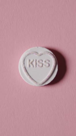 Vertical-Video-Close-Up-Of-Vertical-Video-Of-Hand-Holding-Heart-Candy-With-Meant-To-Be-Message-On-Yellow-Background